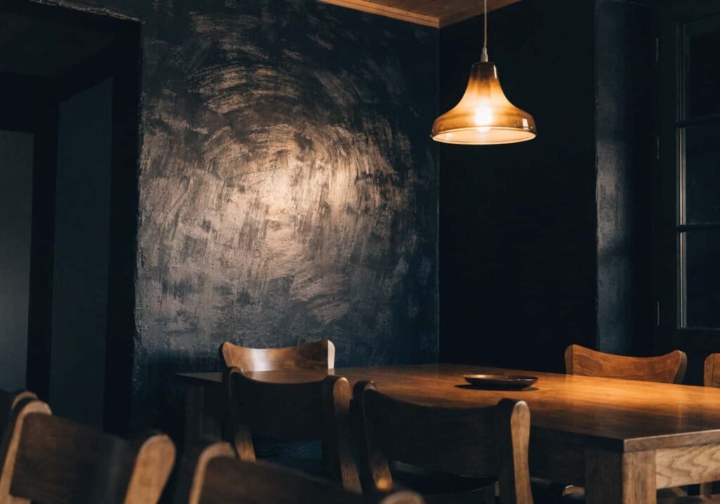 Textured limewash black accent wall with visible depth in a warm, dimly lit dining room.