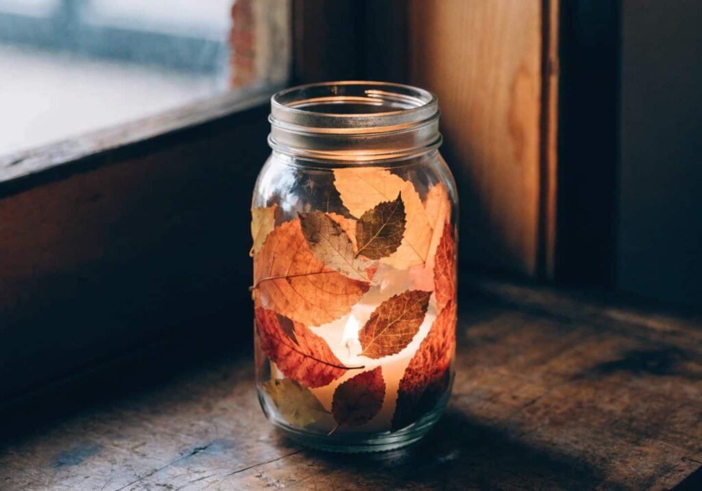 Mason jar covered in pressed fall leaves with a candle glowing inside for autumn table decor