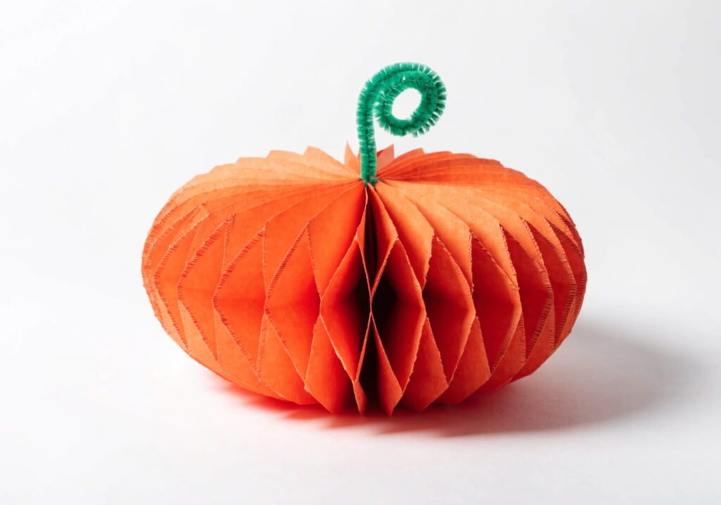 Handmade paper pumpkin craft with textured orange strips and a pipe cleaner stem.