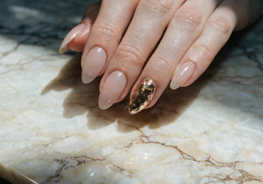 Gold foil accent nail design over a nude polish base