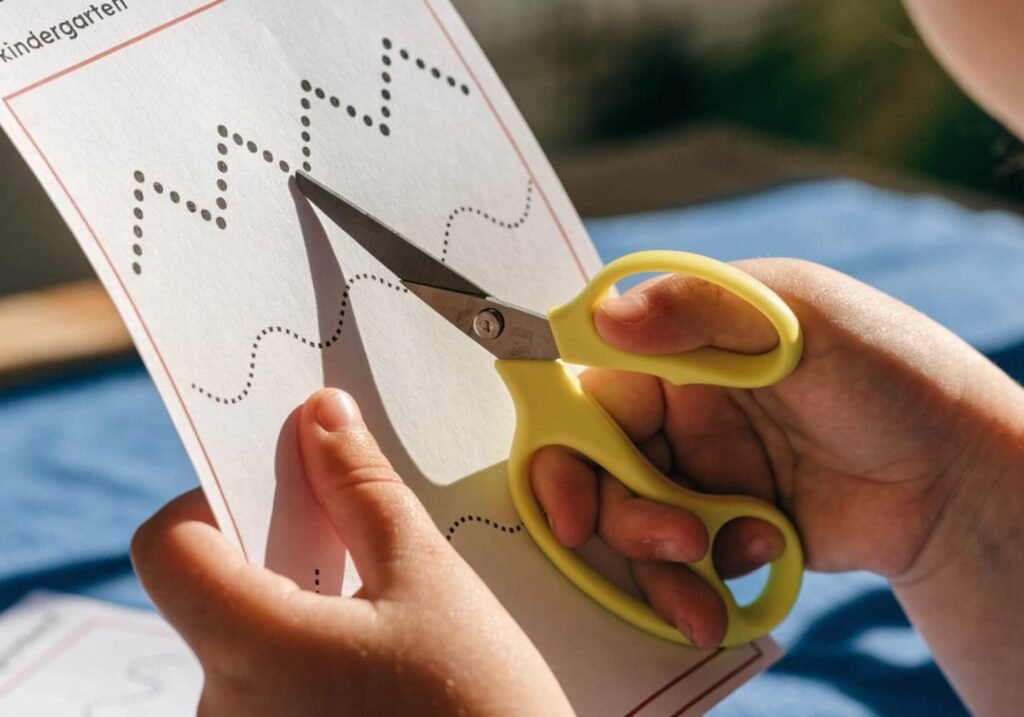 Child practicing cutting skills along zigzag and wavy lines on a kindergarten worksheet.