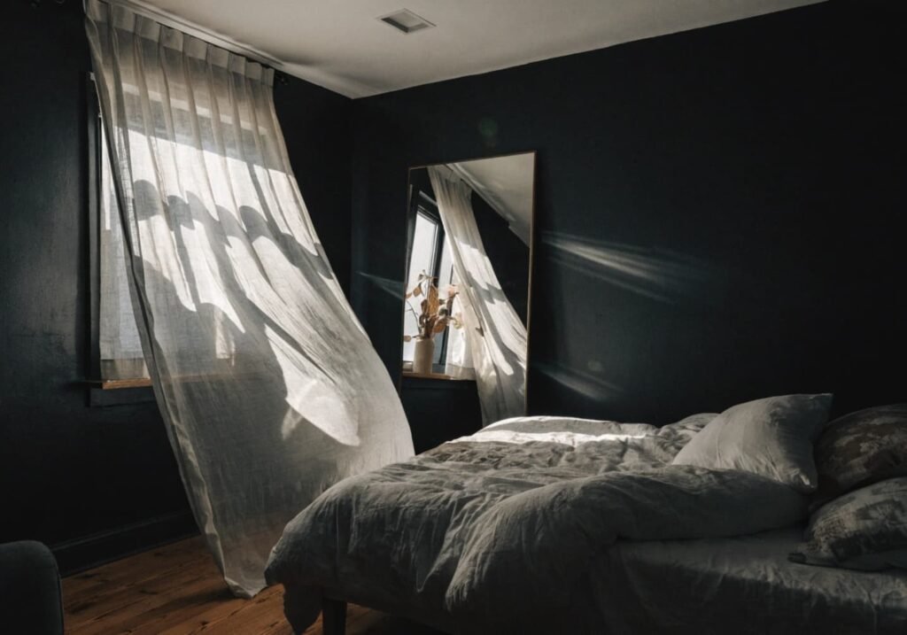 White ceiling and sheer curtains keeping a black-walled bedroom feeling open and airy