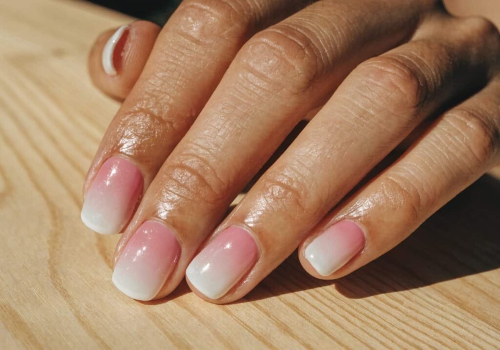Pink to white ombre gradient nails on wooden surface