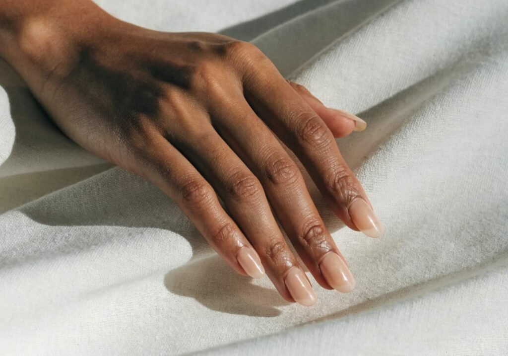 Short almond shape acrylic nails in a nude finish.