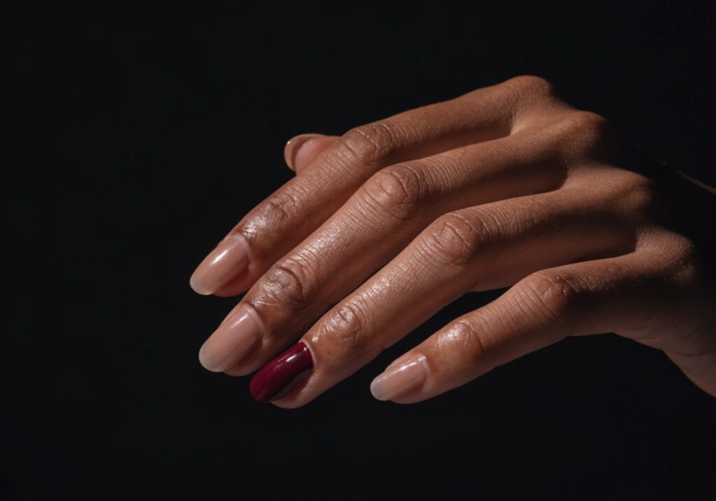 Nude manicure with a single burgundy accent nail on the ring finger.