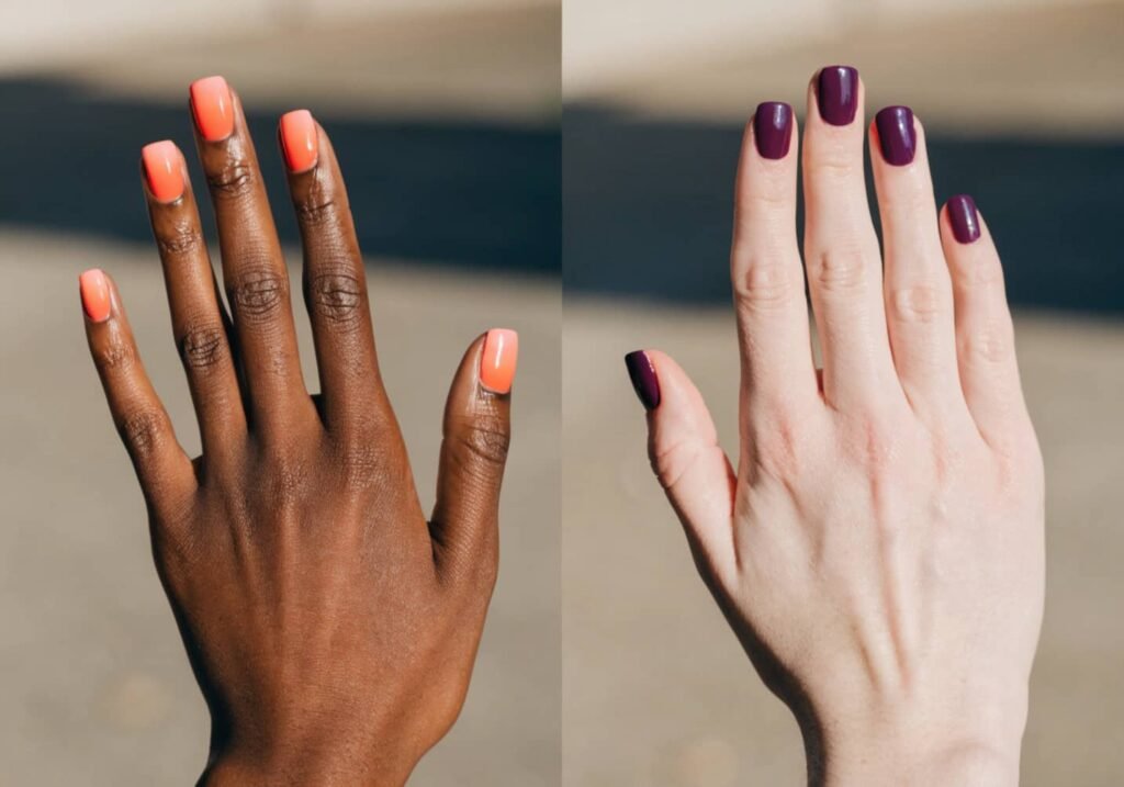 Two hands with coral and berry nail polish comparing skin tone shades