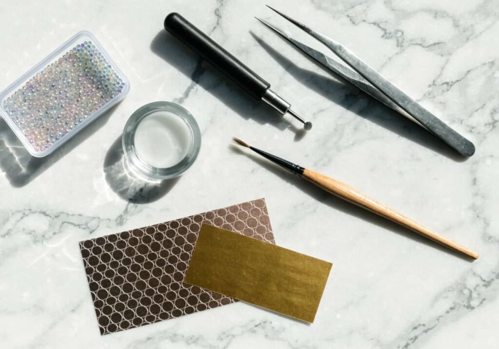 Nail art tools including a dotting tool, detail brush, rhinestones, and foil sheets.