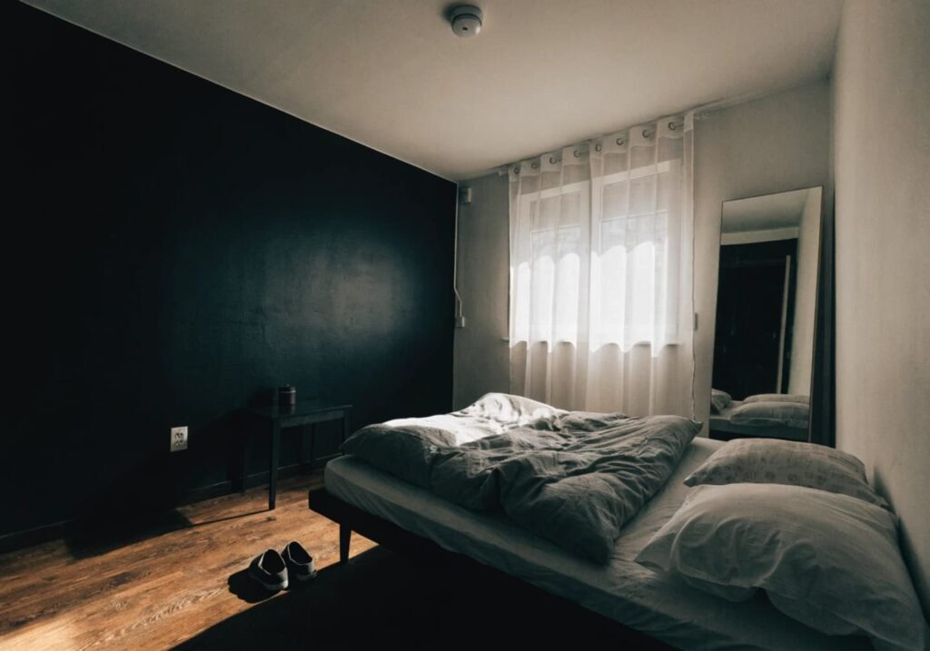 Small bedroom with a black accent wall, low bed, and tall mirror to keep the space open