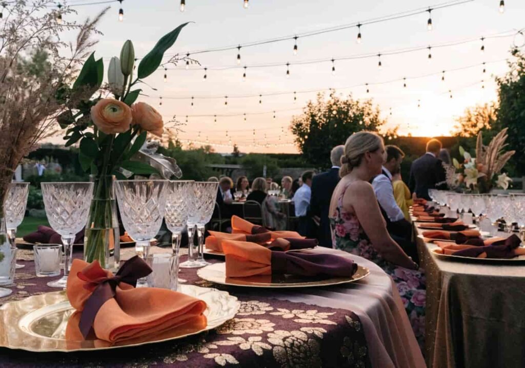 Sunset wedding reception decorated in burnt orange, plum, and gold under warm string lighting.