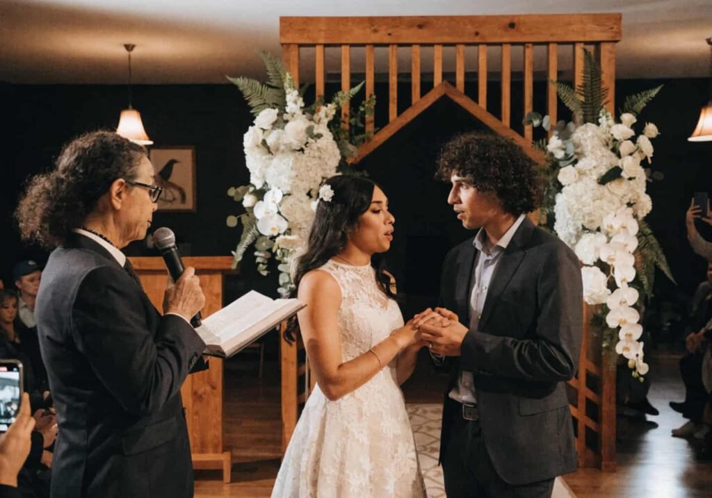 Couple exchanging vows with officiant at indoor wedding altar
