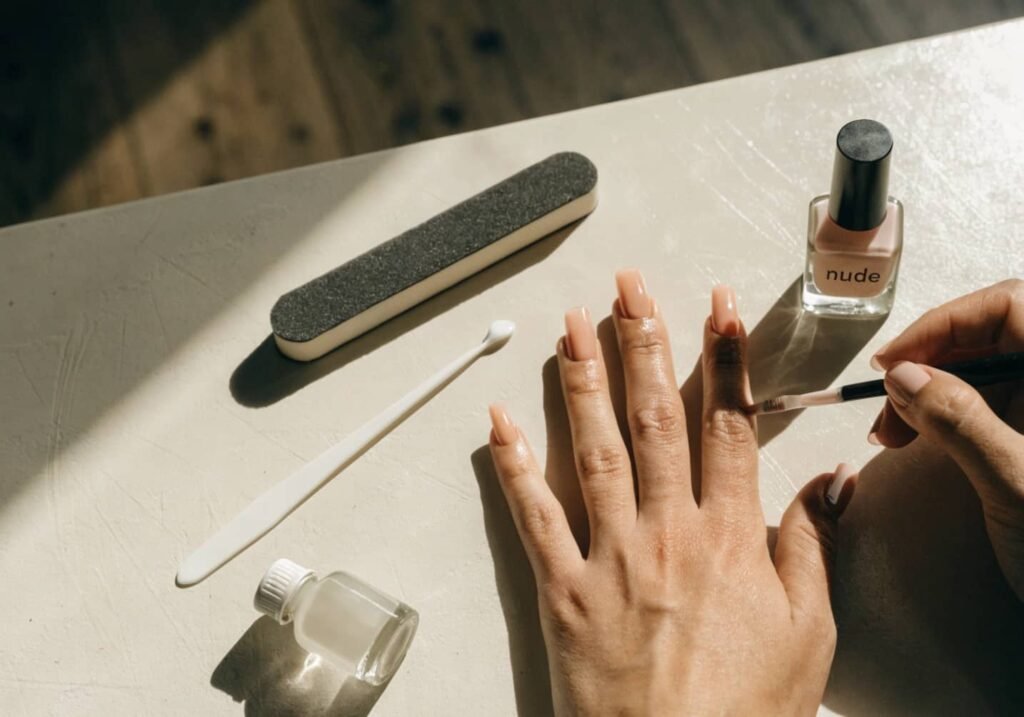 DIY home manicure setup with cuticle pusher, buffer, base coat, and nude nail polish.