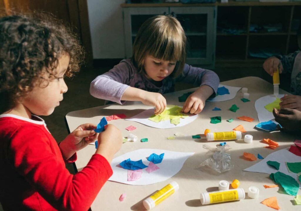 Kindergarten students making a torn tissue paper leaf craft for fine motor skill practice.