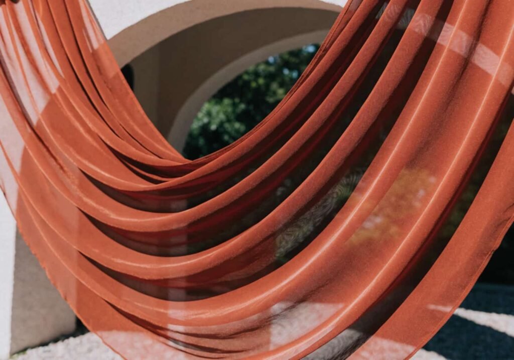 Terracotta chiffon wedding drapery backlit by sunlight showing color shift.