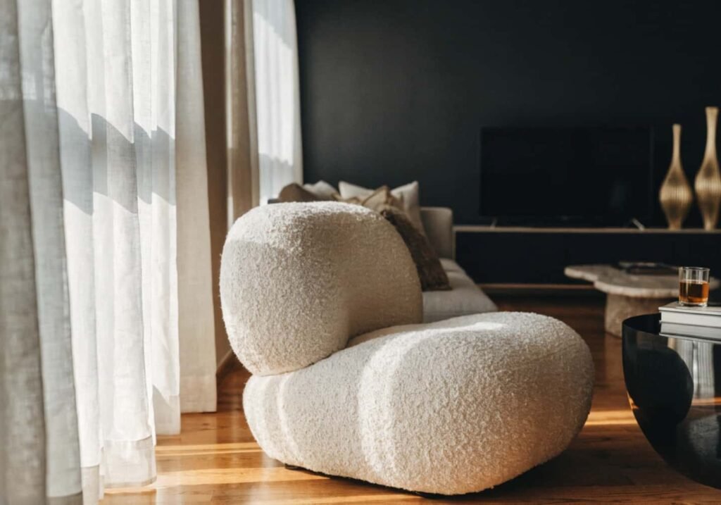 Modern black accent wall softened with sheer curtains and a cream boucle chair for a livable feel.
