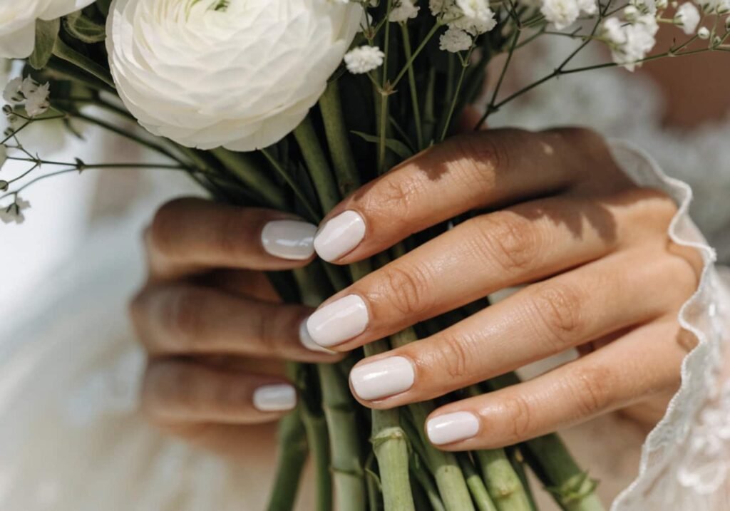 Bridal hand with milky white almond shape acrylic nails holding a bouquet.