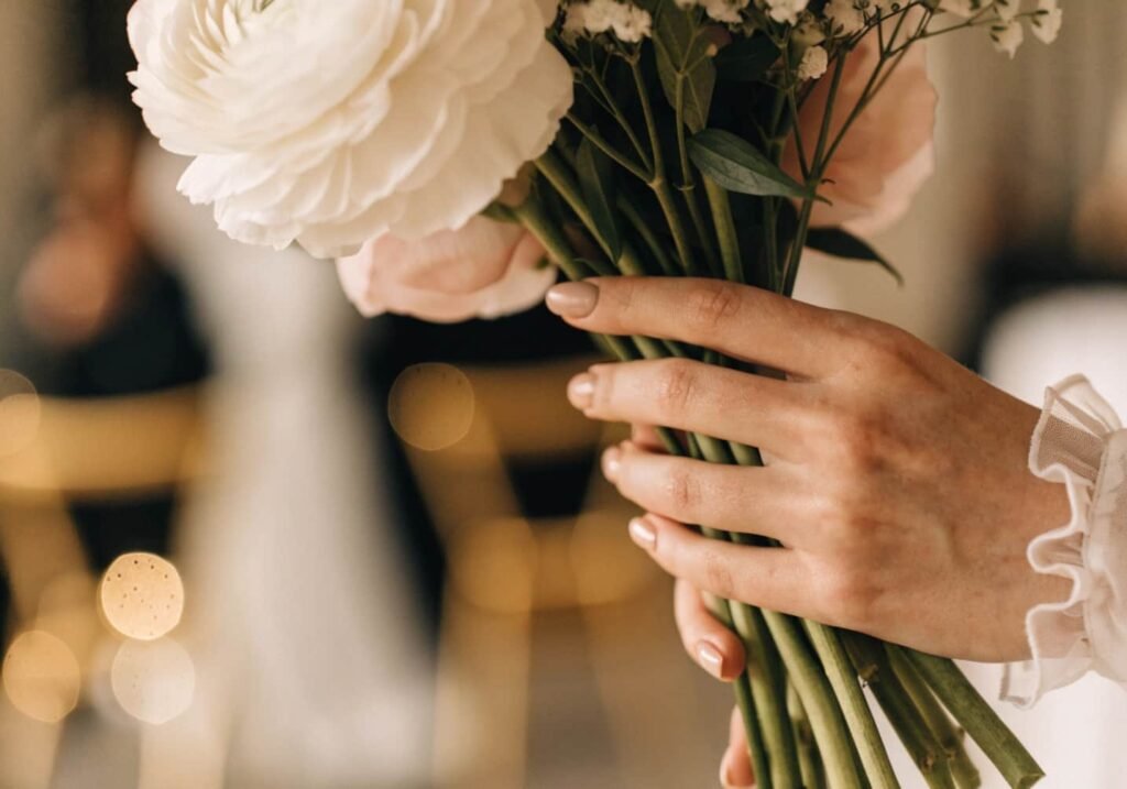 Bride's hand with nude nail polish holding a bouquet