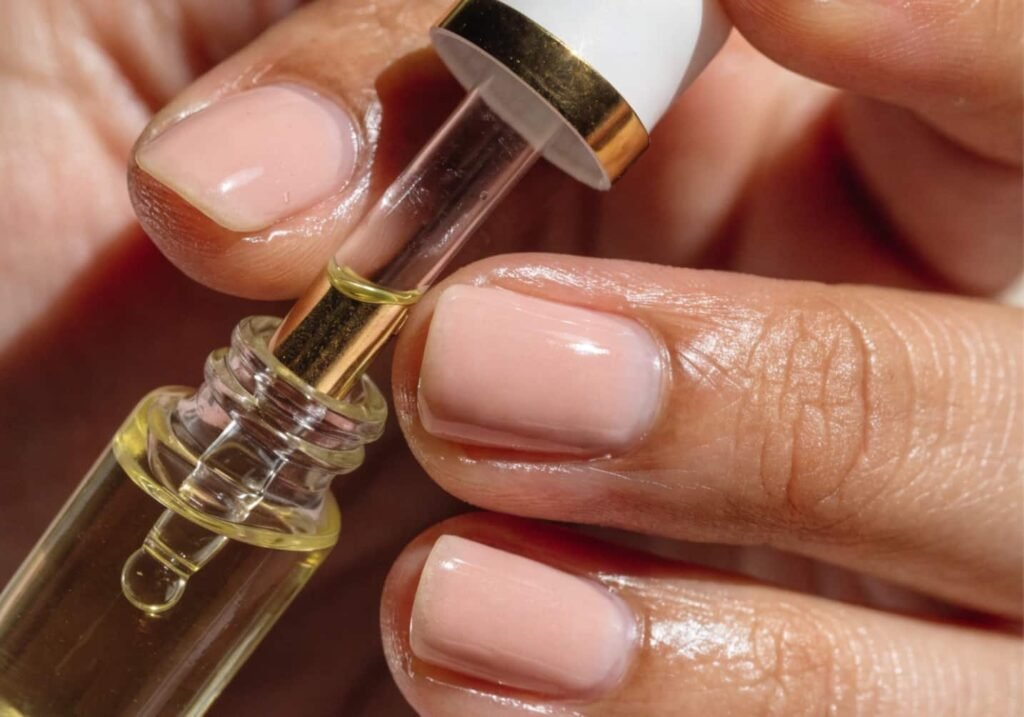 Hand applying cuticle oil to glossy manicured nails