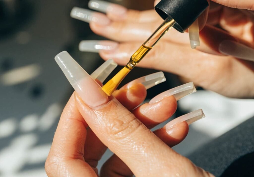 Applying cuticle oil to maintain acrylic nails at home.