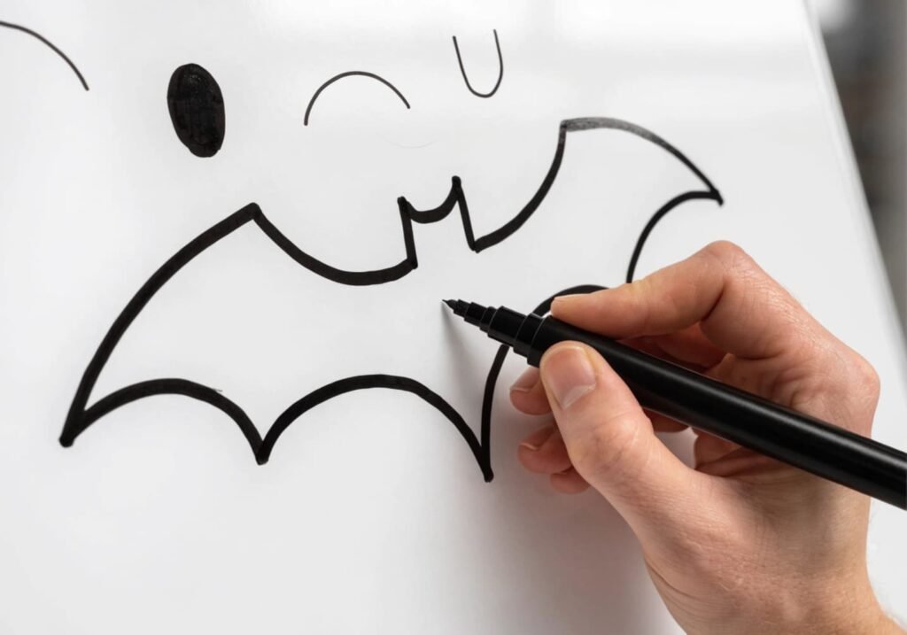 Step-by-step simple bat doodle drawn in black marker on a white board.