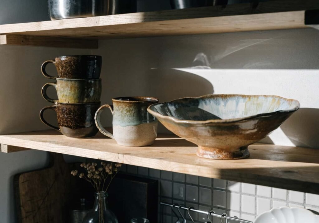 Stoneware pottery mugs and bowl on a kitchen shelf