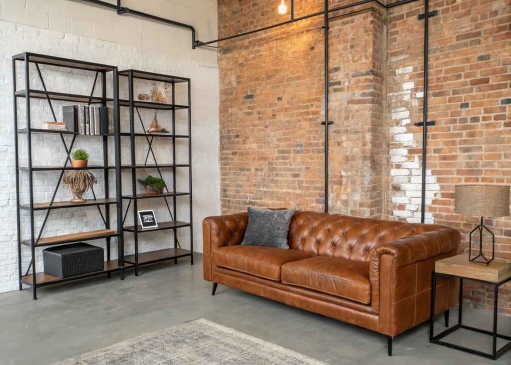 Industrial living room with exposed brick wall, black metal shelving, and a cognac leather sofa