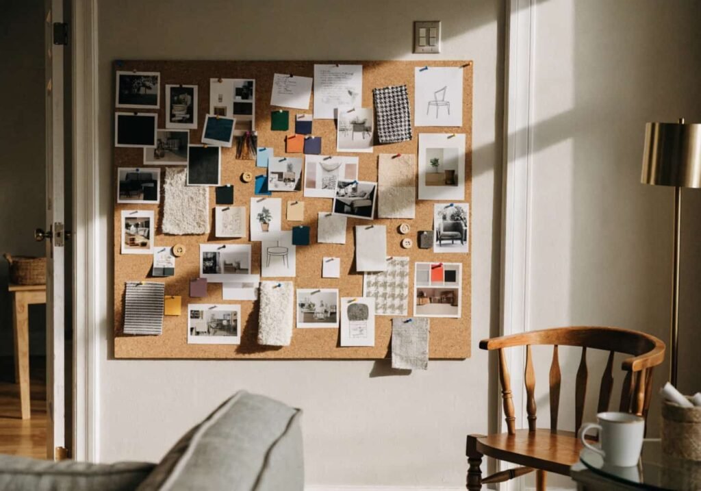 A corkboard mood board with printed decor inspiration photos, fabric swatches, and paint chips pinned together on a living room wall.