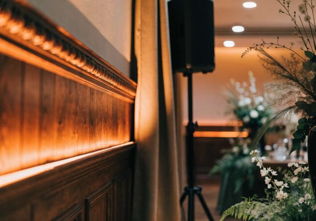 Warm uplighting and speaker setup enhancing an indoor wedding venue.