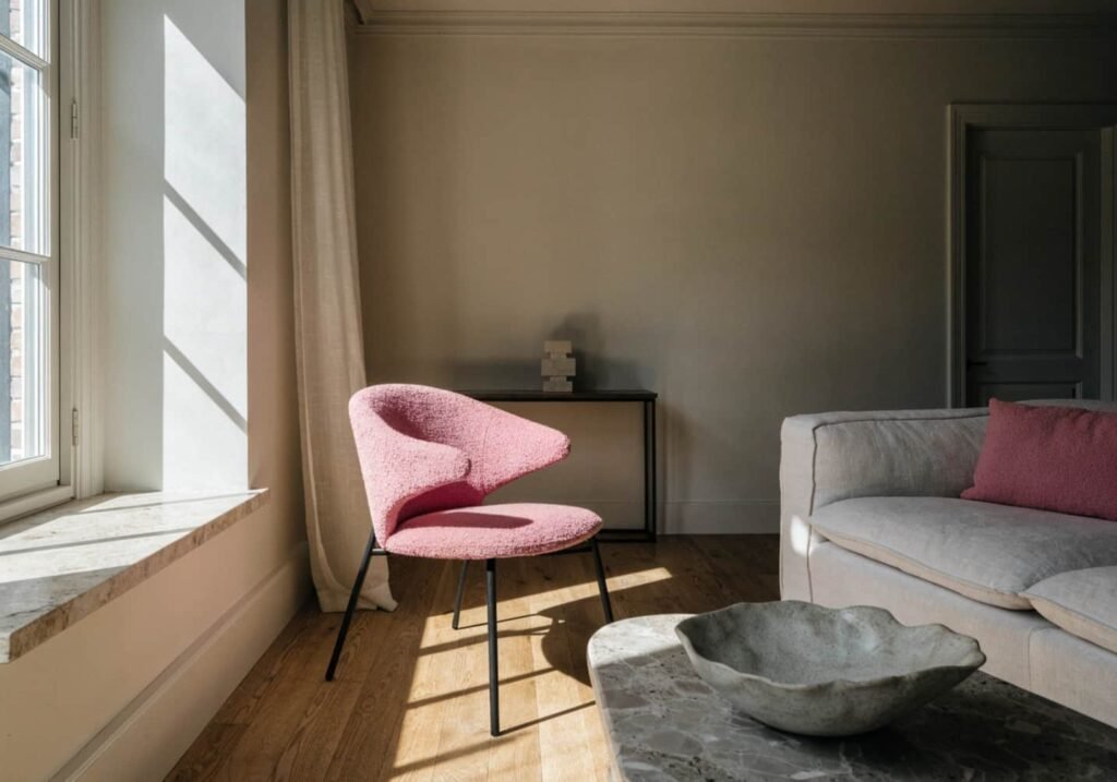 A living room corner showing a restrained pink palette — one pink chair, one pink cushion, no other pink elements.