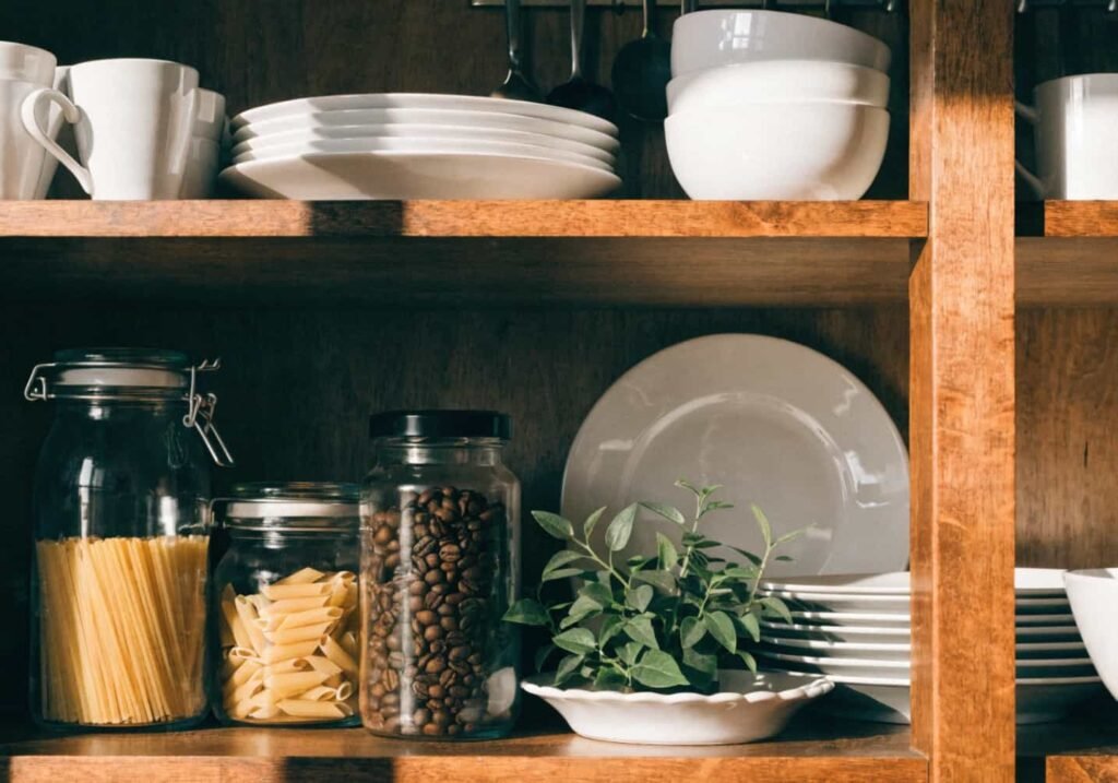 Everyday dishes, jars, and plants styled on an open kitchen shelf.