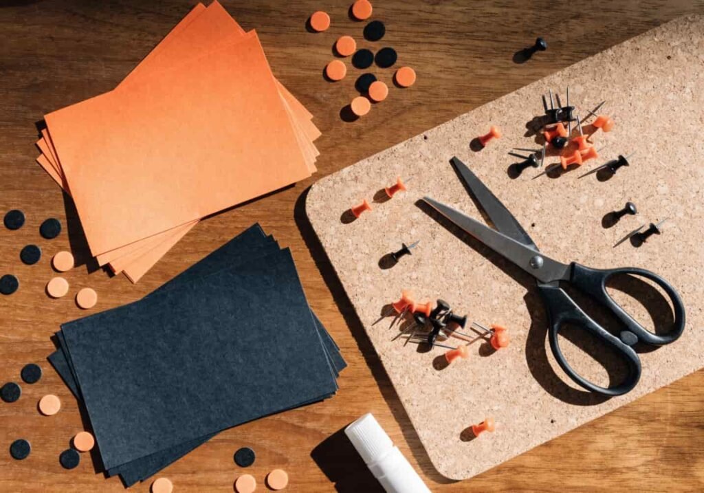 Craft supplies laid out for building a Halloween bulletin board, including cork board, cardstock, and foam dots.