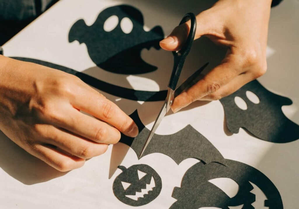 Hand-cutting a black cardstock bat silhouette for a DIY Halloween paper decoration.