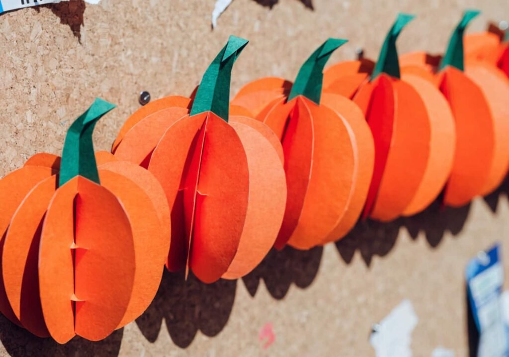 DIY 3D folded paper pumpkins made from orange cardstock for a Halloween board display.