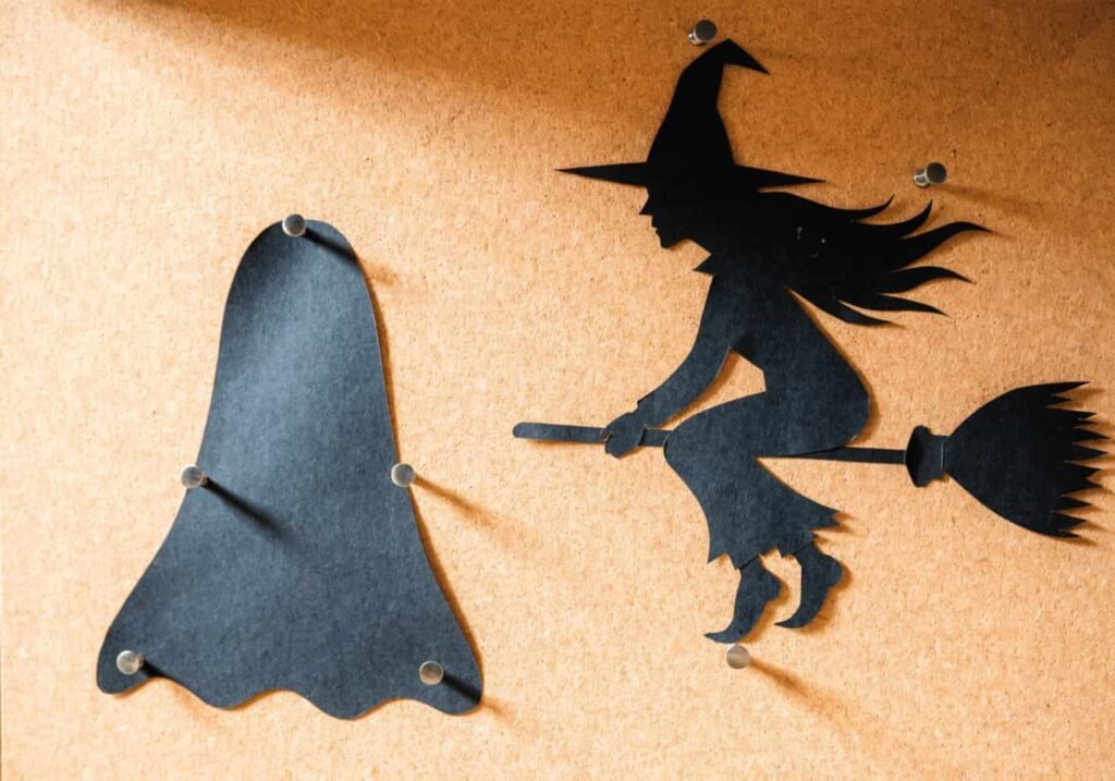 Black cardstock ghost and witch silhouettes displayed on a pale orange Halloween board.