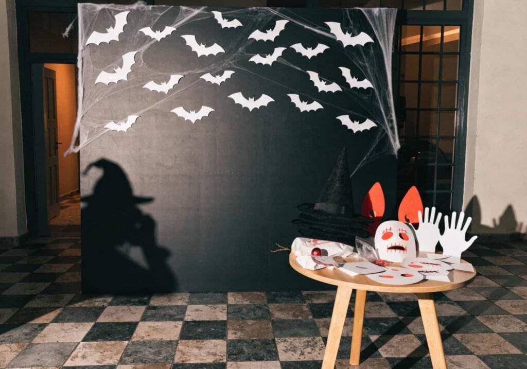 Halloween-themed photo booth backdrop board with props table for guests.