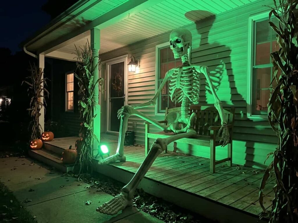 Giant Halloween skeleton on a porch bench lit with green light