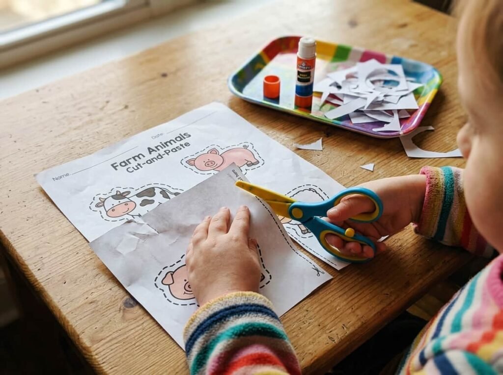 Preschooler using safe scissors on a farm animal cut-and-paste worksheet